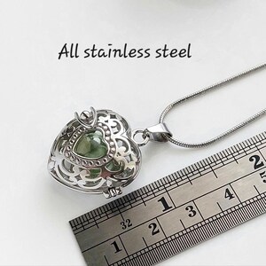 May include: A silver heart-shaped locket necklace with a green glass charm inside. The necklace is made of stainless steel and is 2 inches long. "All stainless steel" is written on a white background.