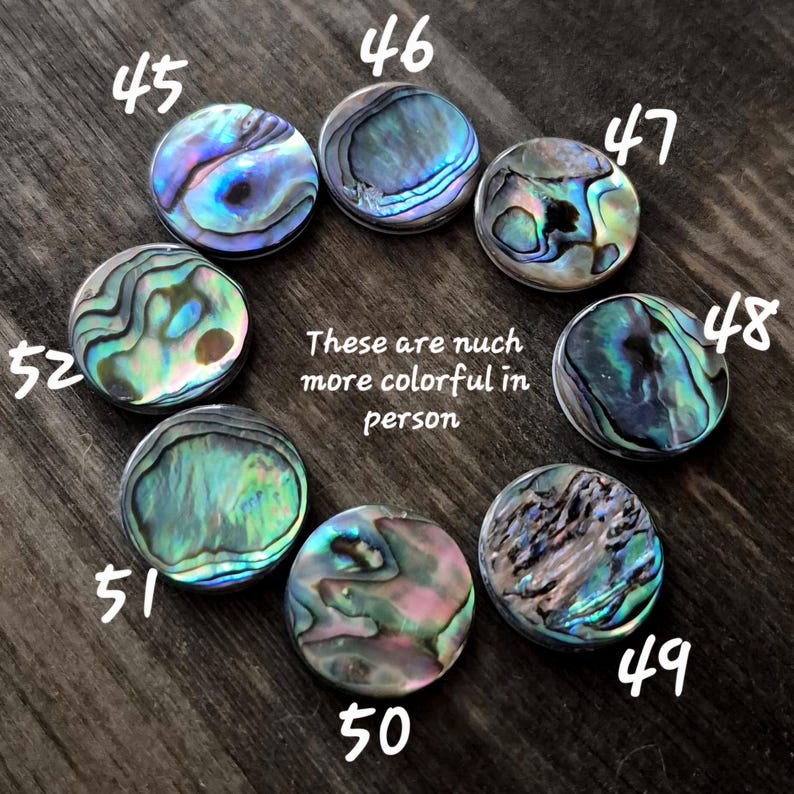 May include: Eight circular abalone shell cabochons arranged in a circle, each featuring unique iridescent patterns of blue, green, and pink. Each piece is labeled with a white number from 45 to 52. Text in the center reads: These are nuch more colorful in person.