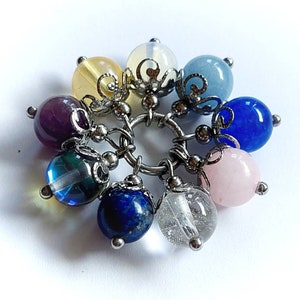 Puede incluir: Un brazalete con dijes con una variedad de cuentas de piedras preciosas de colores, incluyendo amatista, azul, rosa y cuarzo transparente. Las cuentas est&aacute;n unidas a una cadena de plata con detalles met&aacute;licos decorativos.
