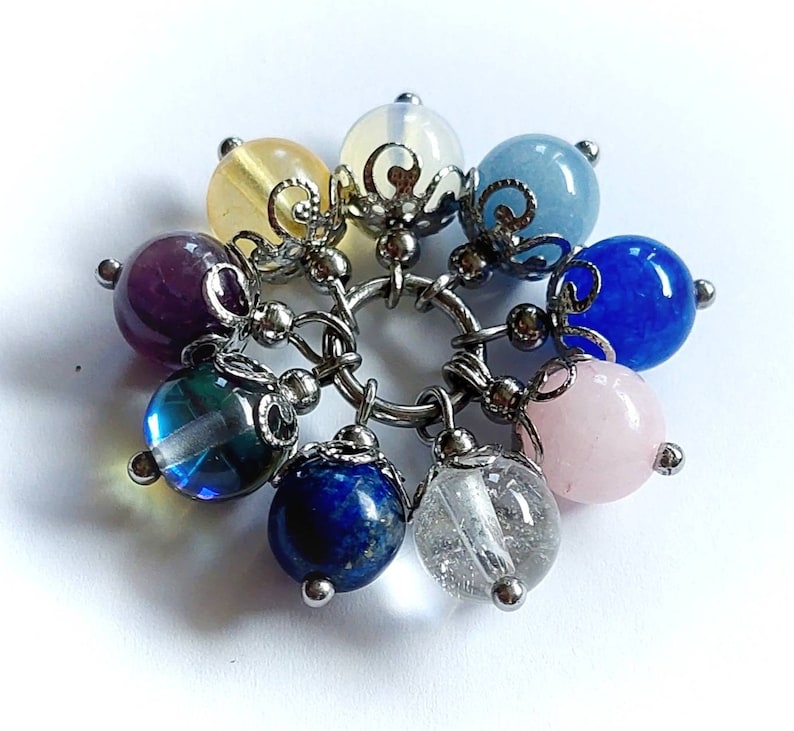Puede incluir: Un brazalete con dijes con una variedad de cuentas de piedras preciosas de colores, incluyendo amatista, azul, rosa y cuarzo transparente. Las cuentas est&aacute;n unidas a una cadena de plata con detalles met&aacute;licos decorativos.