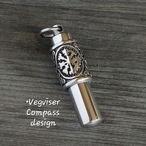 May include: A silver metal pendant with a compass design and a decorative snowflake pattern. The pendant is engraved with the text "Vegviser Compass design".
