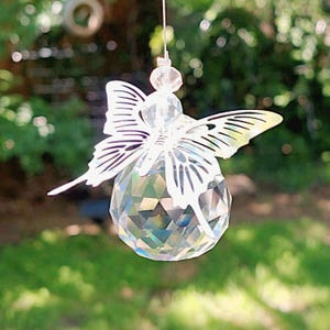 May include: A clear crystal ball suncatcher with a butterfly design. The butterfly has delicate, open wings and is made of a silver-coloured metal. The crystal ball is faceted, reflecting light. The suncatcher is hanging outdoors.