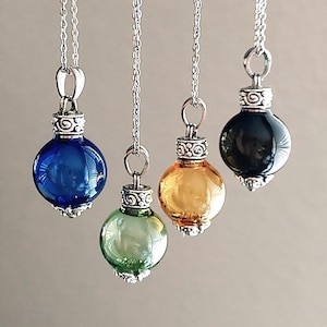 May include: Four glass orb pendants in blue, green, amber, and black, suspended from silver chains. Each orb has a decorative silver cap. The pendants are spherical and reflect light, creating a visually appealing display.