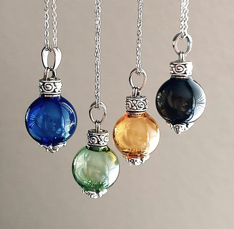 May include: Four glass orb pendants in blue, green, amber, and black, suspended from silver chains. Each orb has a decorative silver cap. The pendants are spherical and reflect light, creating a visually appealing display.