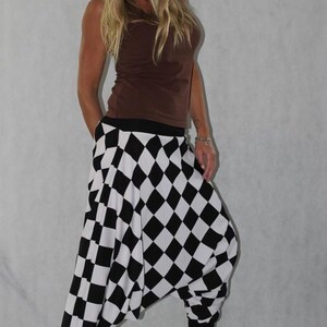 May include: A woman wearing a brown tank top and black and white checkered harem pants. The pants have a wide leg and a loose fit.