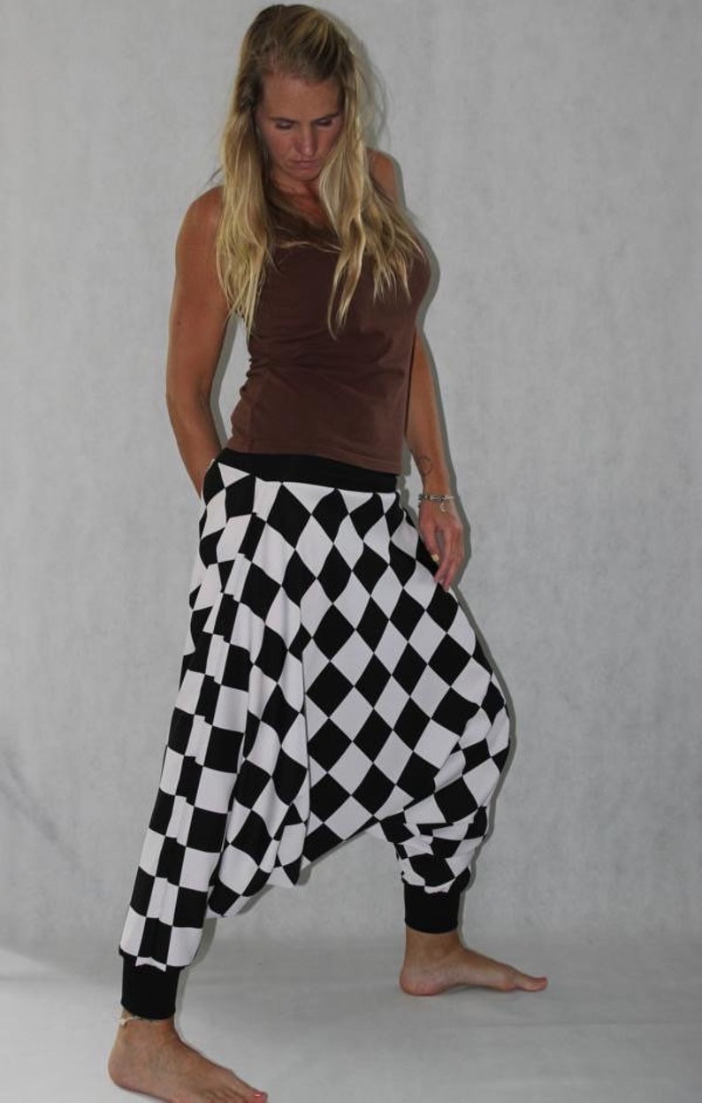 May include: A woman wearing a brown tank top and black and white checkered harem pants. The pants have a wide leg and a loose fit.