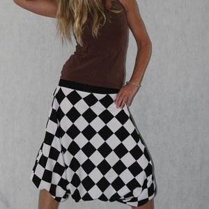 May include: A woman wearing a brown tank top and a black and white checkered skirt. The skirt is a loose-fitting, flowy style.