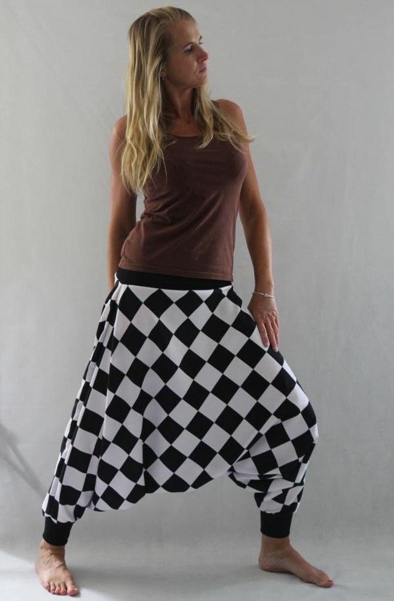 May include: A woman wearing a brown tank top and black and white checkered harem pants. The pants have a wide leg and a gathered waist.