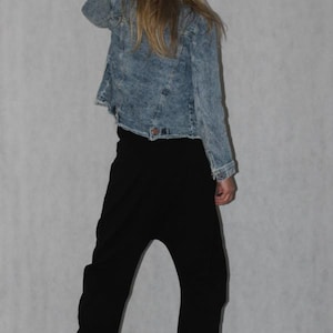 May include: A light blue denim jacket with a faded wash, paired with black drop-crotch pants. The jacket has a classic collar and button closure. The pants have a relaxed fit with elastic cuffs.