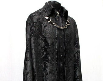 May include: A black cape featuring a tonal damask pattern with a high collar and a silver-toned metal chain closure at the neckline. The garment is displayed on a mannequin, showing a structured fit with intricate fabric detailing.