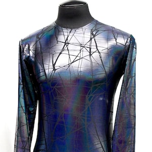 Puede incluir: Una camiseta de manga larga con cuello redondo, con un acabado metálico iridiscente que cambia entre tonos azules, morados y plateados. La tela está cubierta con un patrón geométrico negro, angular y similar a una red en toda la superficie.