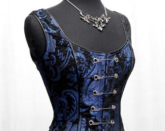 May include: A blue and black corset with a floral pattern and silver safety pin closures. The corset is on a black mannequin and has a black lace skirt.