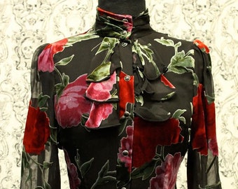 May include: A black sheer blouse with a high collar and long sleeves. The blouse features a velvet floral print in shades of red, pink, and green. The collar has a velvet bow tie.