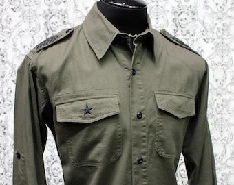 May include: A green long-sleeved button-down shirt with black buttons and a black star on the left pocket. The shirt has a collar and two flap pockets.