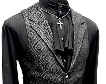 May include: Black formal attire featuring a patterned vest over a black long-sleeve shirt with ruffled cuffs. A silver cross pendant hangs from a chain necklace. The vest has a button-down closure.