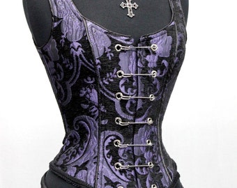 May include: A purple and black brocade corset with a silver chain and cross pendant necklace. The corset has a busk closure and is laced up the back.