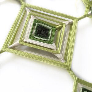 Könnte beinhalten: Ein grüner und weißer Traumfänger mit quadratischem Design. Der Traumfänger besteht aus mehreren Schichten von Schnur, die in der Mitte einen Spiraleffekt erzeugen.