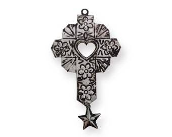 Puede incluir: Una cruz de metal plateado con un corazón recortado en el centro y una estrella colgando de la parte inferior. La cruz está decorada con diseños florales.