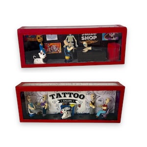 May include: Two miniature tattoo shop dioramas. Each has a red frame and features skeletal figures. One has a sign that reads "TATTOO SHOP". The other has a sign that reads "TATTOO SALON".