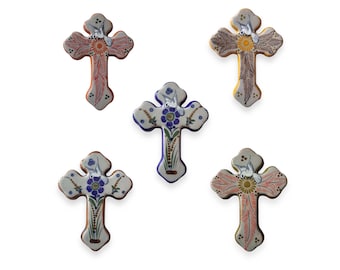 Puede incluir: Cinco cruces de cerámica pintadas a mano con diseños florales y una paloma. Cada cruz está pintada en un esquema de color diferente, incluyendo azul, naranja y amarillo.