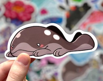May include: A cartoon sticker of a gray and white whale with a cute expression, lying on its side. The sticker has a white outline.