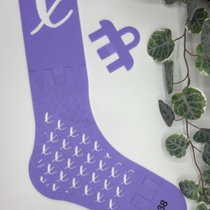 Può includere: Un modello a forma di calzino color lavanda con un design ritagliato e la scritta "Angelica makes". Il modello presenta anche la taglia "37-38". È visibile anche una forma separata abbinata.