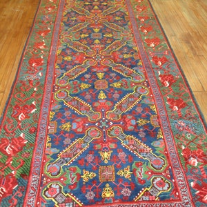May include: A blue and red patterned rug with a floral design. The rug has a border with a green and red floral pattern.
