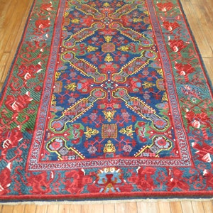 May include: A traditional Persian rug with a deep blue background and intricate floral patterns in shades of red, green, and yellow. The rug has a red border with a repeating floral design.