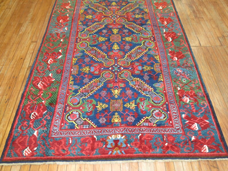 May include: A traditional Persian rug with a deep blue background and intricate floral patterns in shades of red, green, and yellow. The rug has a red border with a repeating floral design.
