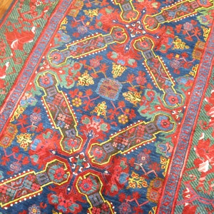 May include: A blue, red, and green patterned rug with a floral design. The rug has a geometric pattern in the center and a border with a floral design.