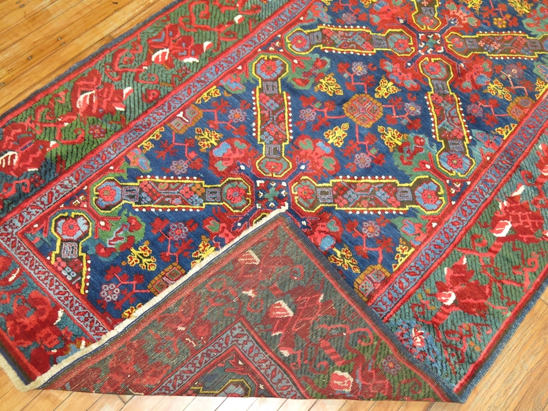 May include: A traditional Persian rug with a blue, red, and green floral pattern. The rug has a fringe border and is folded in half.