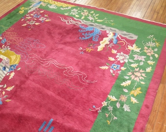 May include: A red rug with a green border. The rug has a floral design with blue, yellow, and white flowers. The rug is made of wool and has a soft texture.