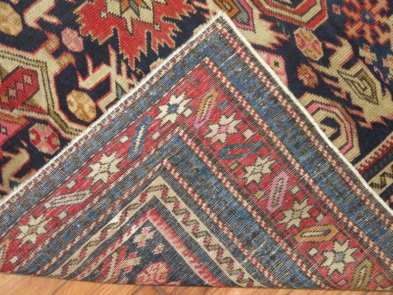 K&ouml;nnte beinhalten: Nahaufnahme einer Ecke eines antiken Teppichs mit dunkelblauem Hintergrund und komplizierten Mustern in Rot-, Rosa-, Beige- und Goldt&ouml;nen.