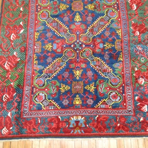 May include: A vintage rug with a blue background and intricate floral patterns in red, yellow, and green. The rug has a red border with a geometric design.