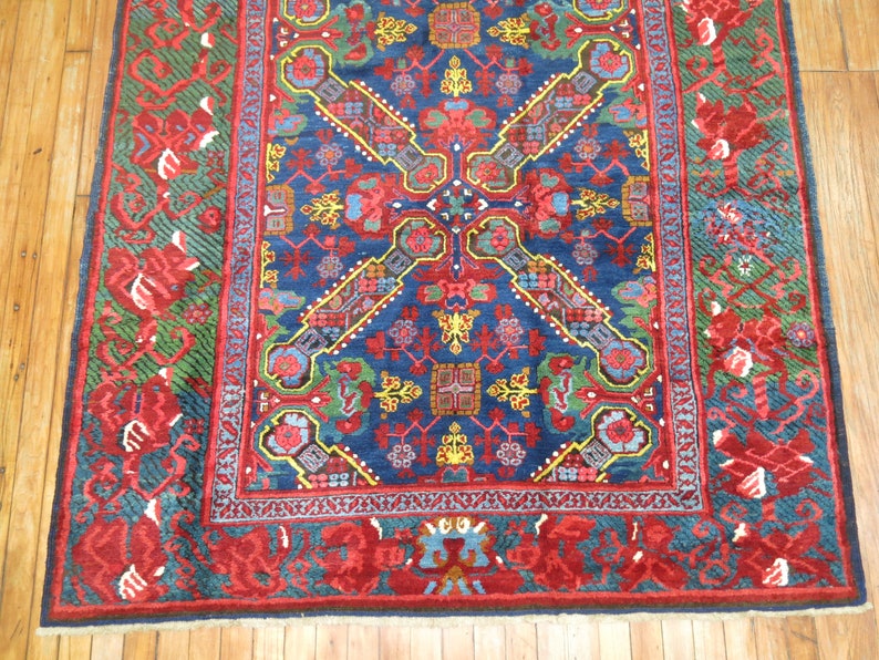 May include: A vintage rug with a blue background and intricate floral patterns in red, yellow, and green. The rug has a red border with a geometric design.