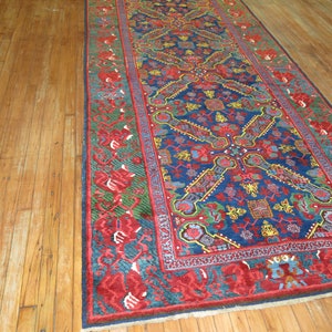 May include: A long, narrow rug with a blue background and intricate floral patterns in red, yellow, and green. The rug has a red border with a floral design.