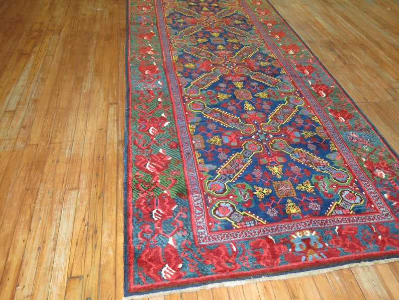 May include: A long, narrow rug with a blue background and intricate floral patterns in red, yellow, and green. The rug has a red border with a floral design.