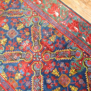 May include: A vintage Persian rug with a blue background and intricate floral patterns in red, yellow, and green. The rug has a border with a repeating pattern of stylized flowers and leaves.