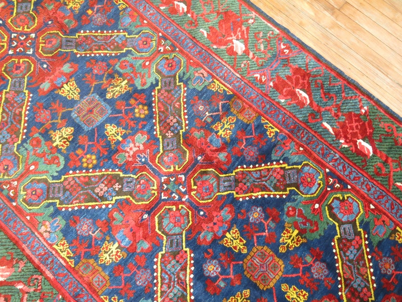 May include: A vintage Persian rug with a blue background and intricate floral patterns in red, yellow, and green. The rug has a border with a repeating pattern of stylized flowers and leaves.