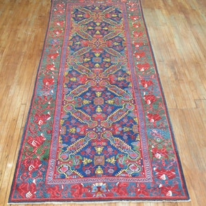 May include: A long, narrow rug with a blue background and a red, green, and yellow geometric pattern. The rug has a fringe border.