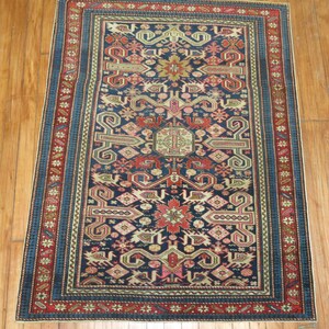 K&ouml;nnte beinhalten: Ein traditioneller t&uuml;rkischer Teppich mit einem dunkelblauen Hintergrund und komplizierten geometrischen Mustern in Rot-, Rosa-, Beige- und Goldt&ouml;nen. Der Teppich hat einen Rand mit einem sich wiederholenden Sternmuster.