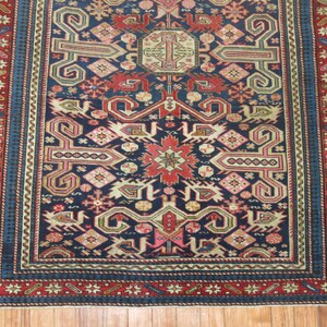 K&ouml;nnte beinhalten: Ein traditioneller Teppich mit dunkelblauem Hintergrund und komplizierten geometrischen Mustern in Rot-, Rosa-, Beige- und Gr&uuml;nt&ouml;nen. Der Teppich hat einen Rand mit einem sich wiederholenden Muster aus Sternen und Blumen.