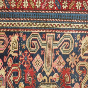 K&ouml;nnte beinhalten: Eine Nahaufnahme eines traditionellen Teppichs mit komplizierten Mustern in Rot-, Blau- und Cremet&ouml;nen. Der Teppich hat ein zentrales Medaillon mit einem geometrischen Muster und floralen Motiven.