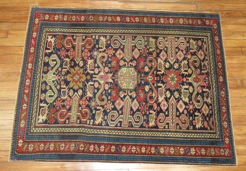 K&ouml;nnte beinhalten: Ein antiker t&uuml;rkischer Teppich mit dunkelblauem Hintergrund und komplizierten geometrischen Mustern in Rot-, Beige- und Cremet&ouml;nen. Der Teppich hat einen Rand mit einem sich wiederholenden Muster aus Sternen und Blumen.