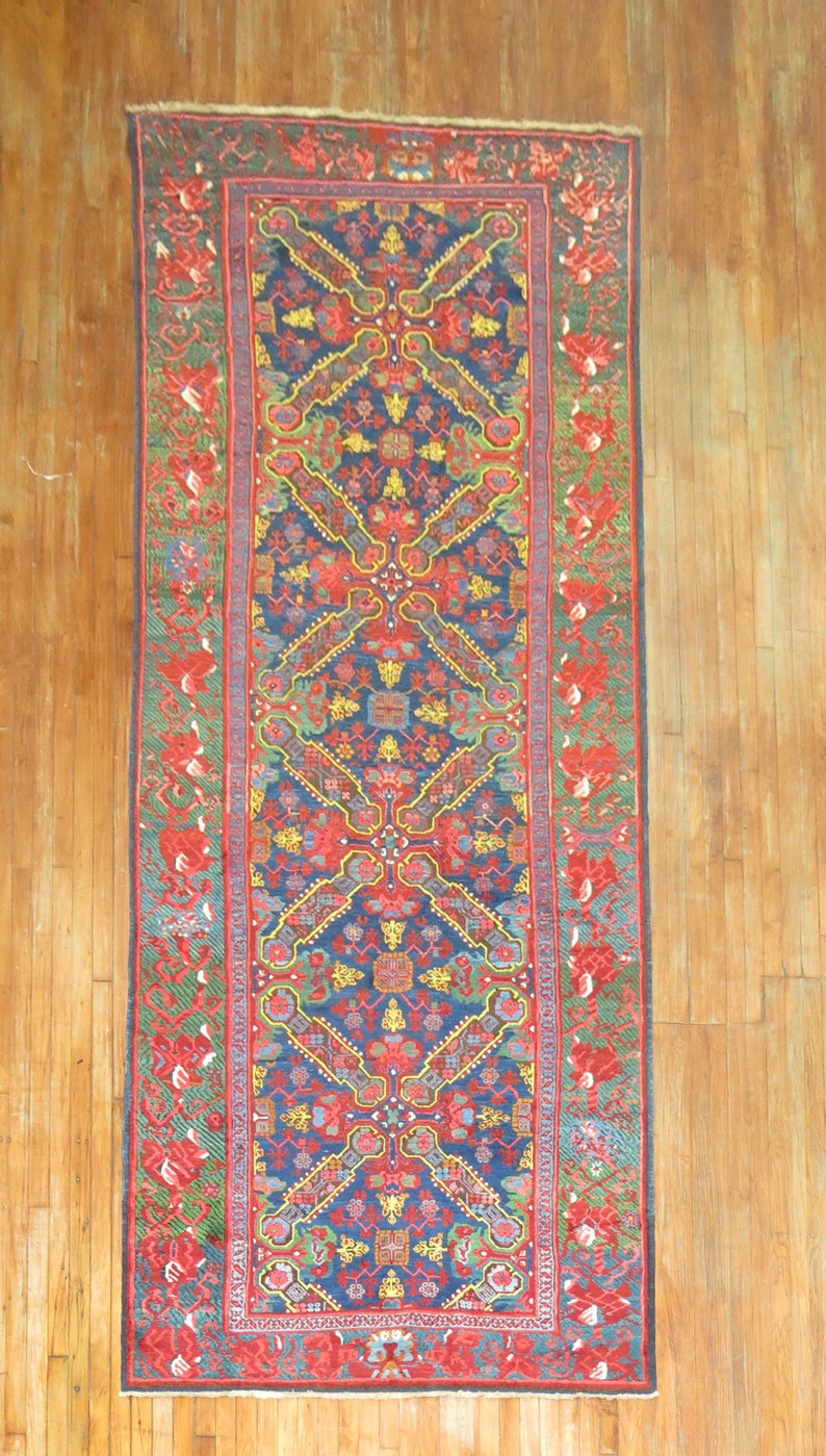 May include: A long, narrow rug with a traditional Persian design. The rug has a dark blue background with intricate patterns in shades of red, yellow, green, and white. The rug is bordered by a red and green floral pattern.