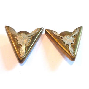 May include: Two triangular metal corner protectors with a brass-toned finish. Each piece features a central silver-toned floral engraving with intricate leaf-like details and a beaded border along the inner edge of the decorative design.