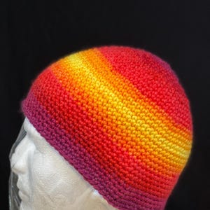 May include: A crocheted beanie hat with a gradient of red, orange, yellow, and purple.