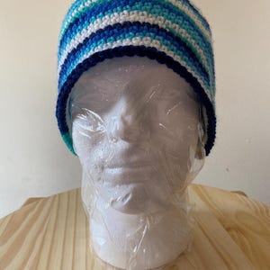 May include: A blue, white and teal striped crocheted beanie hat with a navy blue brim.