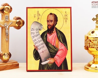 May include: A religious icon featuring a man with a beard holding a scroll with Greek text. The icon has a gold background and is framed in red. A wooden cross and a gold incense burner are on either side.