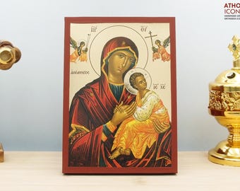 May include: A hand-painted icon of the Virgin Mary and baby Jesus. The icon is on a wooden panel with a red border. The Virgin Mary is wearing a red robe and a blue cloak. She is holding the baby Jesus in her arms. The baby Jesus is wearing a white robe. The icon is surrounded by a gold halo.